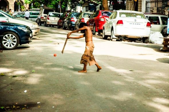 Portrait of a Destitute Playing Cricket with a Stick for the Bat, His Bare Body and a Feverishly Beating Down Sun for Uniform, and a Parking Lot of Super-Expensive Cars for His Field: The Other Side of the Roguish IPL